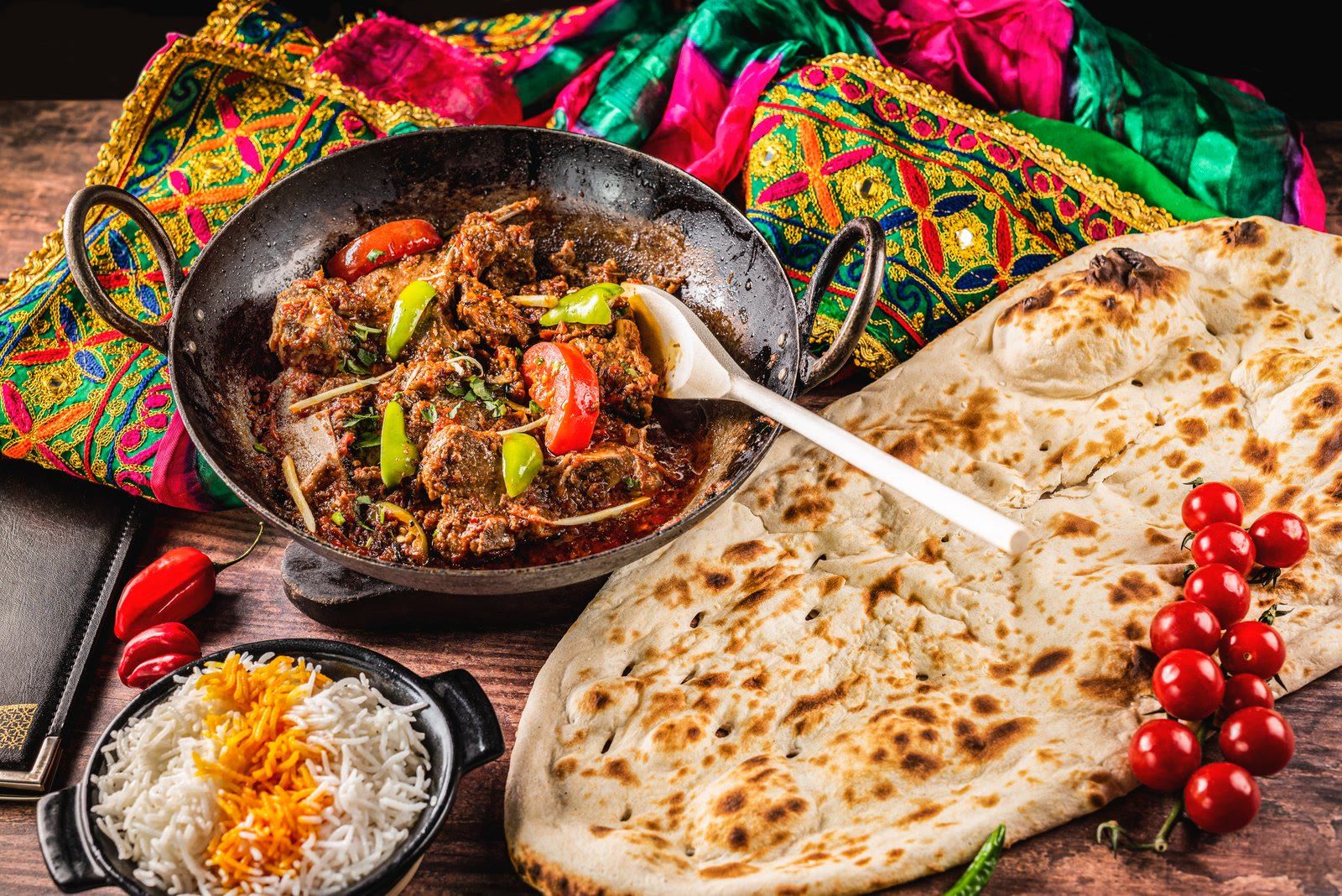 A Spice Village karahi with fresh naan and rice, laid out on embroidered cloth.